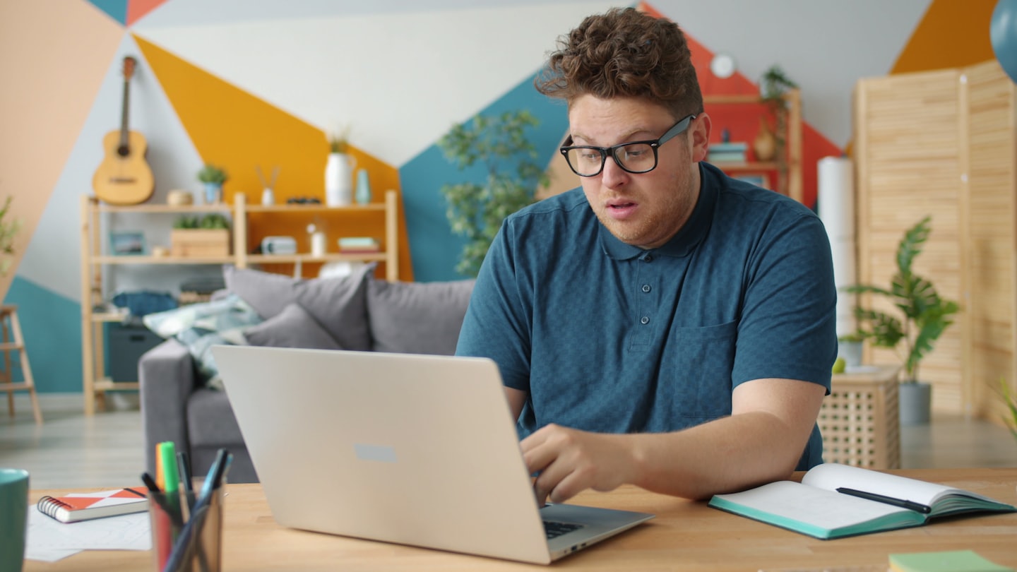 Man wearing glasses works on a laptop at a wooden desk.