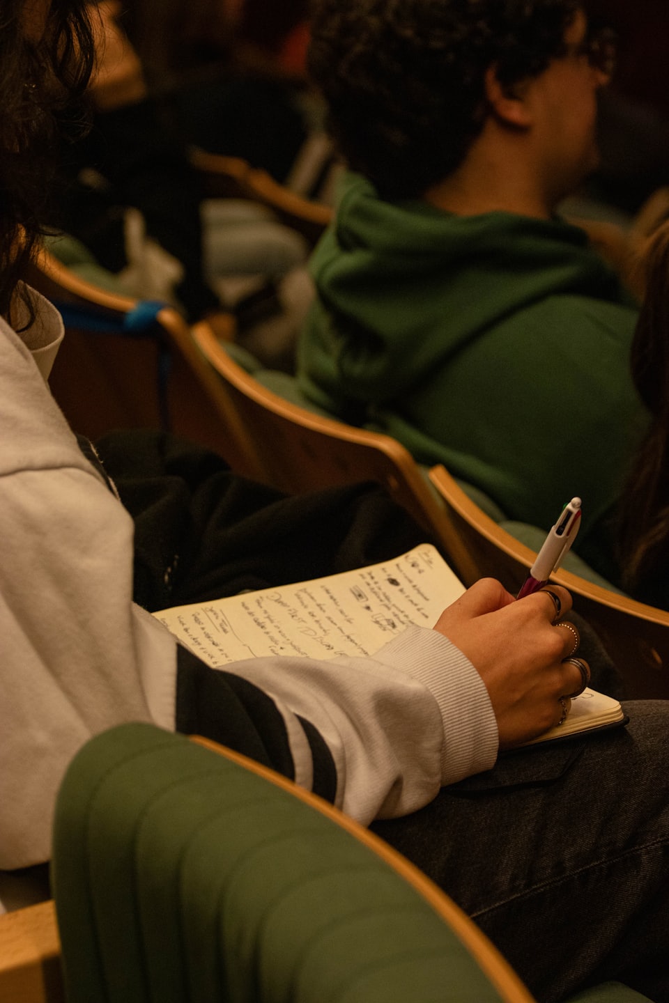Hands writing notes in a notebook during a lecture.